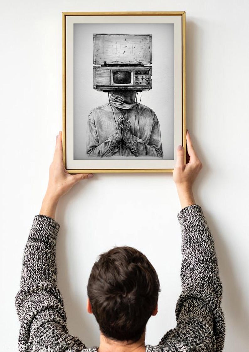 May include: Black and white art print of a person with a vintage radio and television in place of a head. The person is wearing a long-sleeved shirt and has their hands clasped in prayer. The artwork is framed in a gold-colored frame.