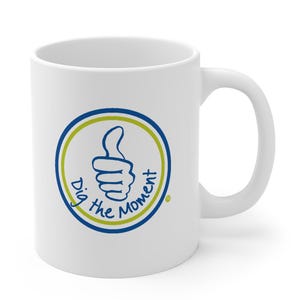 Peut inclure: Une tasse à café en céramique blanche avec un motif circulaire bleu et vert. Le cercle présente un geste de pouce en l'air et le texte "Dig the Moment".