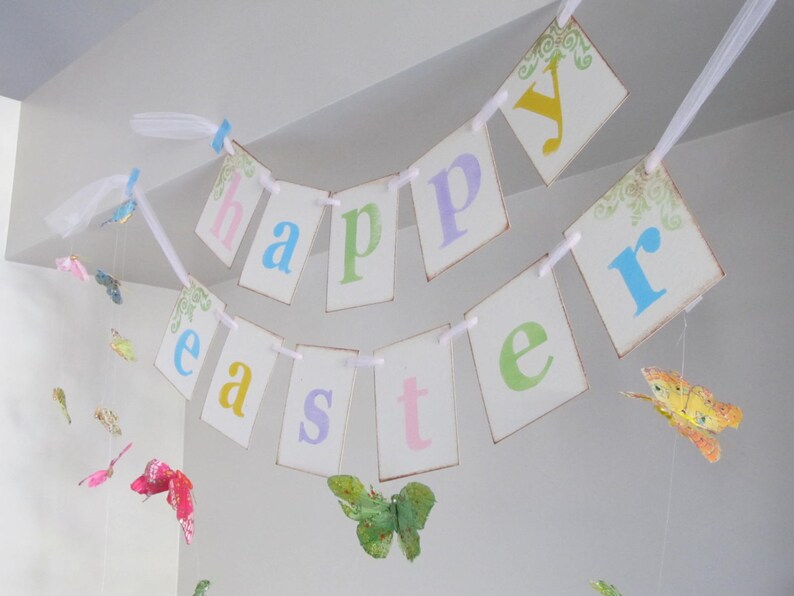 May include: A white banner with the words "happy easter" in pastel colors. The banner is decorated with butterflies and is hanging from the ceiling.