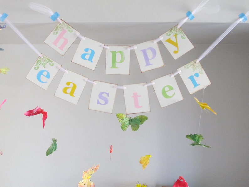 May include: A white banner with the words "Happy Easter" in colorful letters. The banner is strung with white ribbon and decorated with small butterflies.