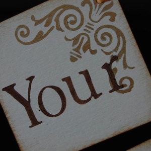 May include: A white sign with brown lettering and a decorative design in the top corner. The sign says "Your".