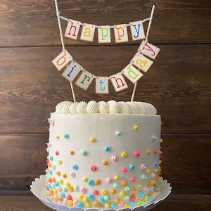 May include: A white cake decorated with colorful sprinkles and a "happy birthday" banner on top.