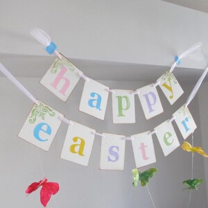 May include: A white banner with the words "Happy Easter" in colorful letters. The banner is decorated with butterflies and is strung up with white ribbon.