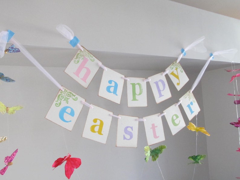 May include: A white banner with the words "Happy Easter" in colorful letters. The banner is decorated with butterflies and is strung up with white ribbon.