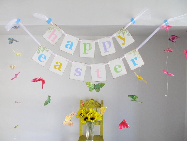 May include: A white banner with the words "Happy Easter" in colorful letters hangs from the ceiling.  Colorful paper butterflies are strung from the ceiling and hang around the banner.