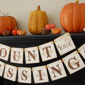 May include: A Thanksgiving banner with the words "Count Your Blessings" in brown letters on a white background. The banner is decorated with fall-themed decorations, including pumpkins, gourds, and pinecones.