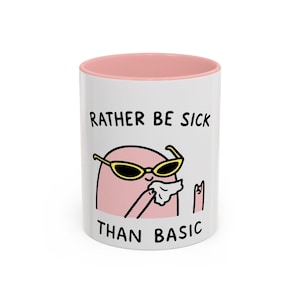 May include: White ceramic mug with a pink interior. The mug features the text "RATHER BE SICK THAN BASIC" with a cartoon illustration of a pink blob wearing sunglasses and holding a tissue.