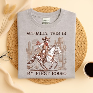 Actually, This Is My First Rodeo T-Shirt | Funny Western Graphic Tee | Raccoon Quote | Retro Shirt Unique Gift Idea | Unisex Shirt