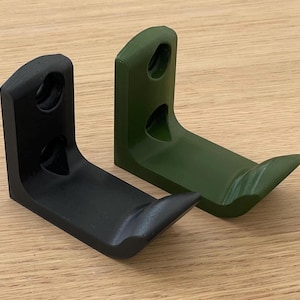 Op de afbeelding: Twee wandhaken, een zwarte en een groene, zijn gemaakt van plastic en hebben een gebogen vorm. Ze zijn ontworpen om aan een muur te worden gemonteerd.