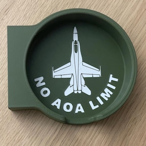 Op de afbeelding: Een groene ronde onderzetter met een wit silhouet van een straaljager en de tekst "NO AOA LIMIT" rond de straaljager.