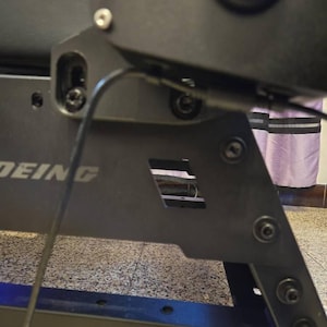 May include: Close-up of a black metal frame with the word "DEING" printed on it. The frame has several screws and a black wire running through it.