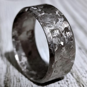 Puede incluir: Un anillo de plata con una superficie texturizada. El anillo está hecho de material de meteorito.
