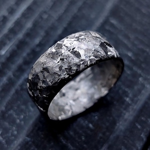Puede incluir: Un anillo de plata con un acabado martillado y texturado. El anillo es ancho y tiene un perfil redondeado.