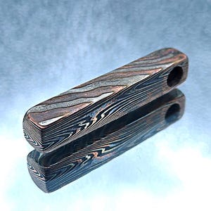 May include: A rectangular pendant featuring a layered mokume gane pattern with alternating bands of copper, brass, and nickel silver. The metal bar has a smooth, polished finish and a single circular hole drilled near one end for suspension.