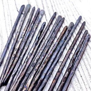 以下が含まれることがあります： 暗いグレーのハンマーで叩かれた金属製のヘアピン18本セット。ピンは扇形に配置され、表面にテクスチャがあります。