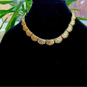 May include: A gold-tone woven necklace with a scalloped design. The necklace is on a black velvet background.