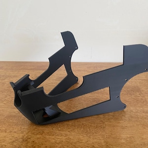 May include: Black plastic 3D printed object with a geometric design. The object has a curved shape and appears to be a stand or support.