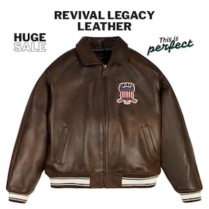 May include: A brown leather jacket with a zip-up front, a collar, and a patch on the chest. The jacket has white and brown striped cuffs and hem. The text "REVIVAL LEGACY LEATHER" is at the top.