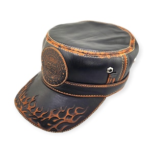 May include: Black leather cap with a flat top and a short brim. The cap features a skull emblem and flame designs in brown. Brown stitching and trim detail the cap's edges. A metal accent is on the side.
