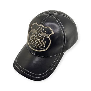 May include: Black leather baseball cap with white stitching. The cap features a metal emblem that reads "US ARMY VETERAN" with stars and a banner. The hat has a curved brim and a classic six-panel design.