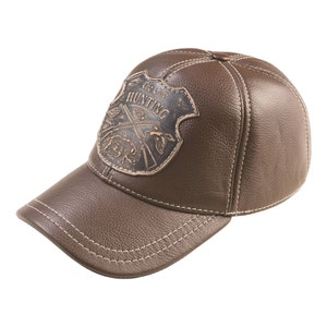 May include: A brown leather baseball cap with a stitched brim and a brown leather patch on the front that says "The Club Hunting" with a hunting scene.