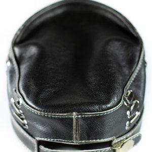 May include: A black leather baseball cap with a silver buckle and stitching around the brim.