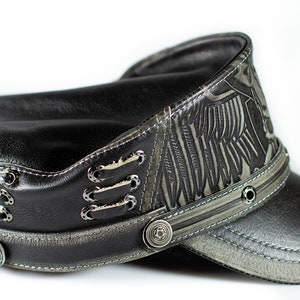 May include: A black leather cap with a gray patterned design and a black leather brim. The cap has a silver buckle and metal accents.