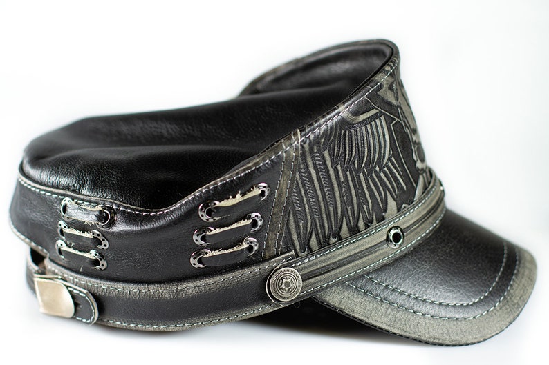 May include: A black leather cap with a gray patterned design and a black leather brim. The cap has a silver buckle and metal accents.