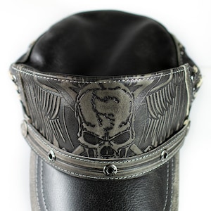May include: A black leather cap with a skull and wings design. The cap has a stitched brim and metal rivets.