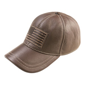 Puede incluir: Gorra de béisbol de cuero marrón con visera curva y diseño cosido. La gorra presenta un parche rectangular con un diseño de bandera estadounidense desgastada. Costuras blancas.