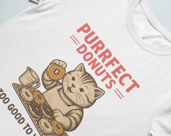May include: White t-shirt featuring a cartoon cat wearing an apron and holding a donut. The shirt has the text "PURRFECT DONUTS" and "TOO GOOD TO WASTE" in red. The cat is surrounded by donuts.