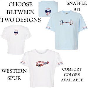 May include: Two short-sleeve t-shirts, one light blue and one white, featuring graphic prints. The light blue shirt displays a snaffle bit with a red, white, and blue pattern. The white shirt shows a western spur with a similar patriotic design.