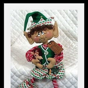 May include: A handmade elf doll with a green hat, red and white striped pants, and a green vest. The elf is holding a small doll and has a tag that says "Merry Christmas".