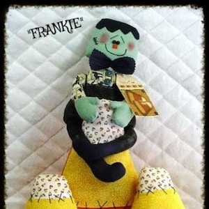 May include: A handmade Halloween decoration featuring a Frankenstein's monster figure and two candy corn pieces. The Frankenstein figure is green with black hair and a bow tie. The candy corn pieces are yellow, orange, and white.
