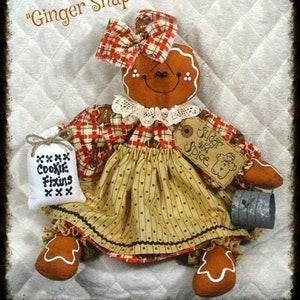 May include: Gingerbread doll wearing a red and white plaid dress with a brown and white polka dot skirt. The doll is holding a bag that says "Cookie Fixins" and a tin that says "Sugar and Spice".