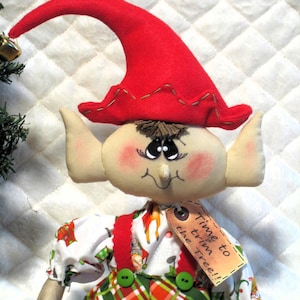 May include: A handmade elf doll with a red pointed hat and large ears. The doll has a painted face with rosy cheeks and is wearing a patterned shirt, red suspenders, and green plaid pants. A tag reads "Time to trim the Tree!!".