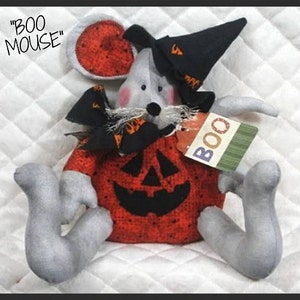 May include: A gray plush mouse dressed as a pumpkin for Halloween. The mouse is wearing a black witch hat and a red and black pumpkin costume with a jack-o-lantern face. The mouse has a tag that says "BOO" on it.