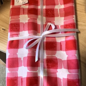 May include: A folded fabric with a red and pink checkered pattern, tied with a white ribbon. The fabric has a tag with handwritten numbers. The pattern is a mix of light and dark shades of red and pink.
