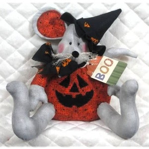 May include: A gray and white plush mouse dressed as a pumpkin for Halloween. The mouse is wearing a black witch hat and a black and orange scarf. The pumpkin costume has a black jack-o'-lantern face and the mouse is holding a tag that says "BOO".