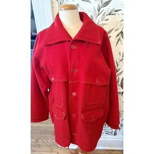 May include: A bright red wool coat with a large collar, button-up front, and multiple pockets. The coat has a classic design, suitable for cold weather. The coat is displayed on a mannequin.