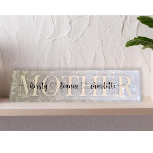 May include: White glass plaque with the word "Mother" in raised letters and the names "Kirsty", "Leanne", and "Charlotte" written below. The names are separated by small hearts.