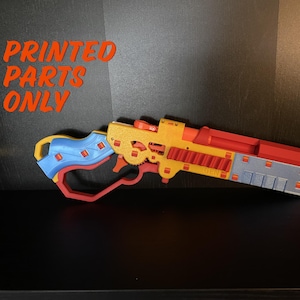 May include: A 3D printed toy gun with a blue, red, and yellow color scheme. The gun has a barrel with a series of small, rectangular holes. The text "PRINTED PARTS ONLY" is visible in the image.
