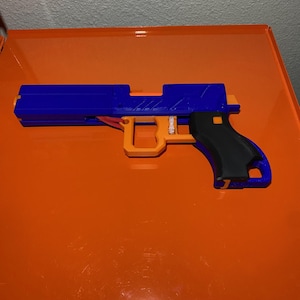 May include: A blue and orange toy gun with a black handle. The gun is made of plastic and has a textured surface.
