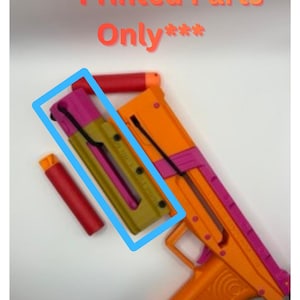 May include: A colorful toy gun with orange, pink, and yellow components. The image includes the text "Printed Parts Only". The gun has a magazine and a barrel. The toy is designed with a trigger and a handle.