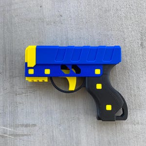 May include: A blue and yellow toy gun with a black handle. The gun has a textured surface and a yellow trigger.