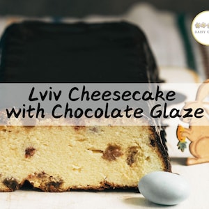 May include: A Lviv cheesecake with a chocolate glaze. The cheesecake is cut in half, revealing a light yellow interior with brown flecks. The cheesecake is on a wooden cutting board with a blue and white Easter egg.