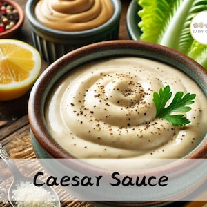 Op de afbeelding: Een close-up van een kom met romige Caesar-salade dressing met zwarte peper en een takje peterselie erop. De kom staat op een houten oppervlak met een citroenwig en een lepel met zout op de achtergrond.