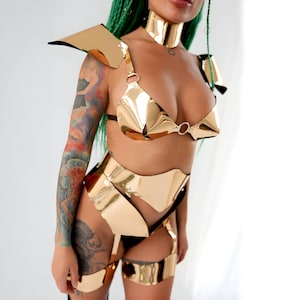 May include: A gold-colored, metallic, body suit with a bra top, a skirt, and thigh-high leg pieces. The suit has a geometric design.