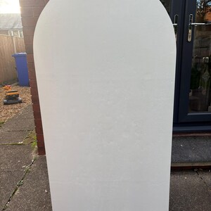 May include: A large, off-white, arched-top panel. The panel has a rectangular base and a rounded top. The surface has a textured appearance. The panel is standing upright on a stone surface.