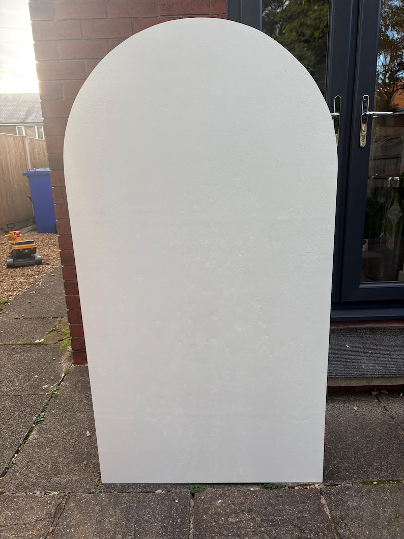 May include: A large, off-white, arched-top panel. The panel has a rectangular base and a rounded top. The surface has a textured appearance. The panel is standing upright on a stone surface.